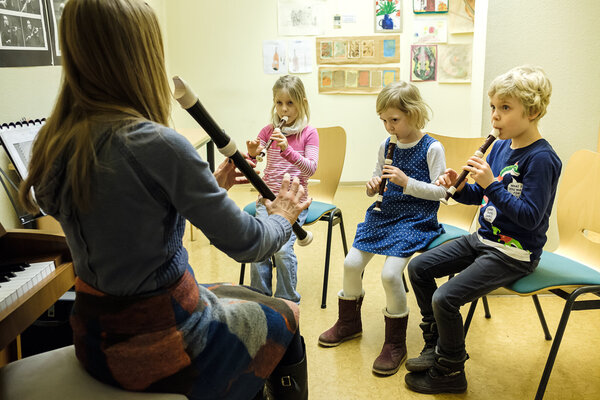 Drei Kinder spielen zusammen mit ihrer Lehrerin Blockflöte.