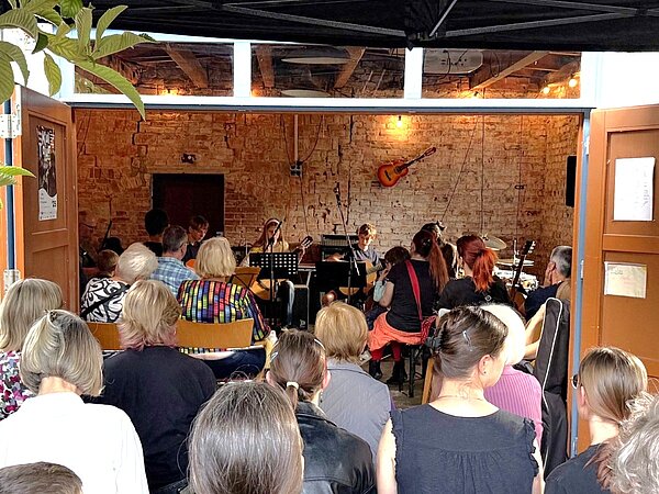 Die Musikschüler spielen in der KulturgarageRadebeul bei gedimmten Licht Gitarre vor einem sitzenden Publikum.