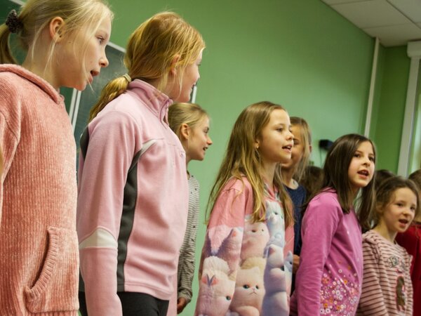 Mädchen singen in einem Chor. Sie stehen vor einer Tafel im Klassenzimmer.