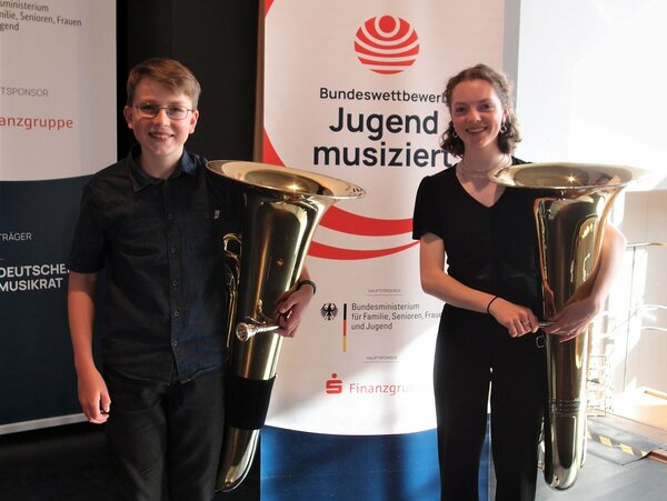 Das erfolgreiche Blechblas-Duo posiert vor dem Banner von Jugend musiziert, Bundeswettbewerb.