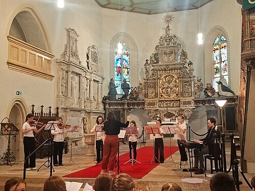 Ein junges Ensemble spielt im Kirchenraum vor dem Altar, vor Publikum.