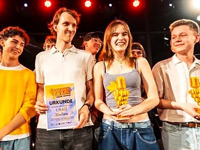 Die vier Bandmitglieder von "30er Zone" lächeln stolz, mit ihrem Wettbewerbspokal von Golden Grape Music Contest, in die Kamera.