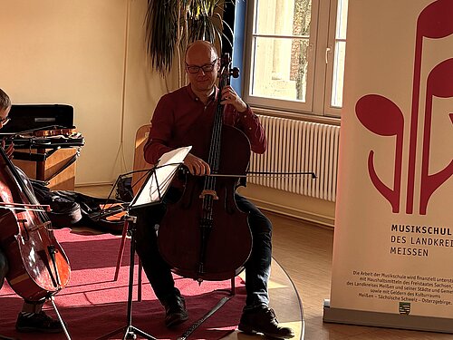 Ein Lehrer musiziert zusammen mit seinem Schüler. Beide spielen Cello.