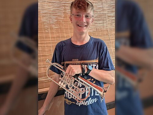 Erfreut über die Aufnahme in das Landesjugendorchester Sachsen lächelt der Musikschüler Max Schubert mit seiner Trompete in der Hand in die Kamera.
