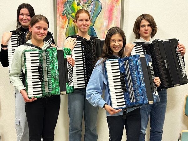 Fünf Akkordeonschüler posieren mit ihren Instrumenten, vor einem gemalten Bild, für die Kamera.