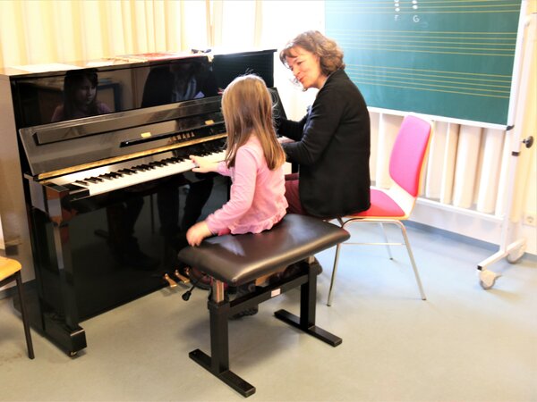 Ein Kind probiert unter Anleitung das Klavier aus.