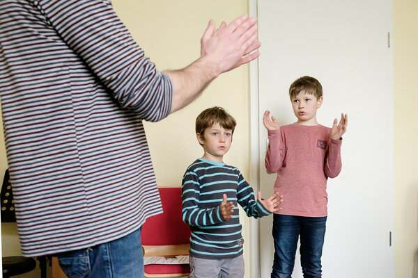 Zwei Kinder und ein Lehrer stehen im Raum und Klatschen.