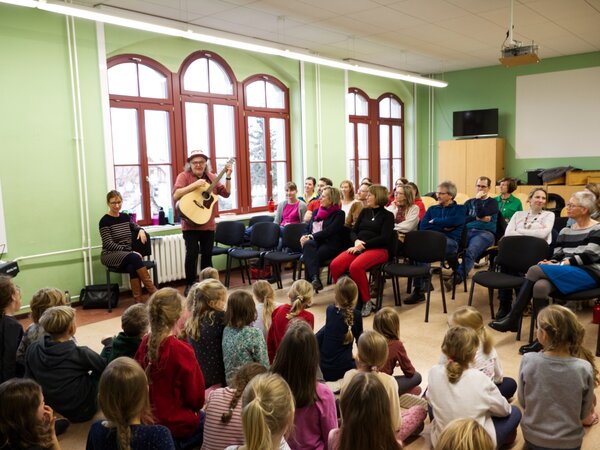 Gerhard Schöne in Aktion mit anwesenden Kindern, Eltern, Chorleiterin Annegret Stämmler und Kultusministerin von Sachsen Barbar Klepsch.