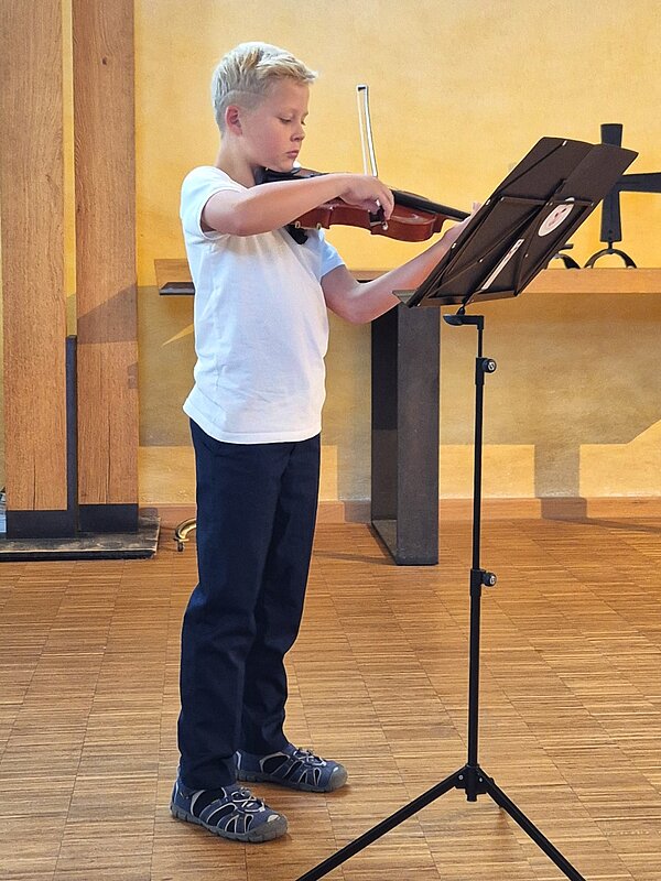 Ein junger Geigen Schüler steht seitlich vor seinem Notenpult und musiziert.