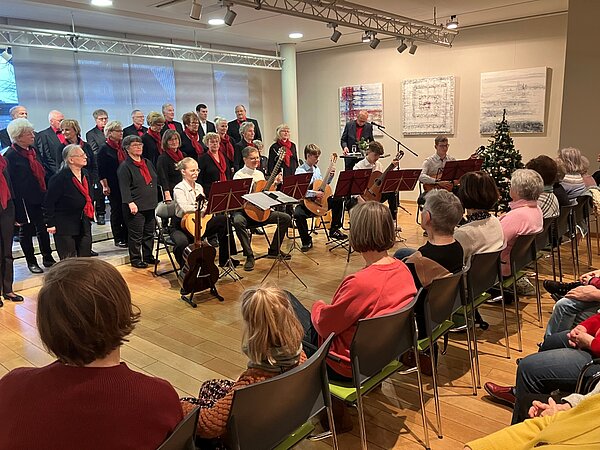 Ein Gitarrenensembles sitzt und spielt, dahinter steht ein Chor. Das Publikum hört gespannt zu. 