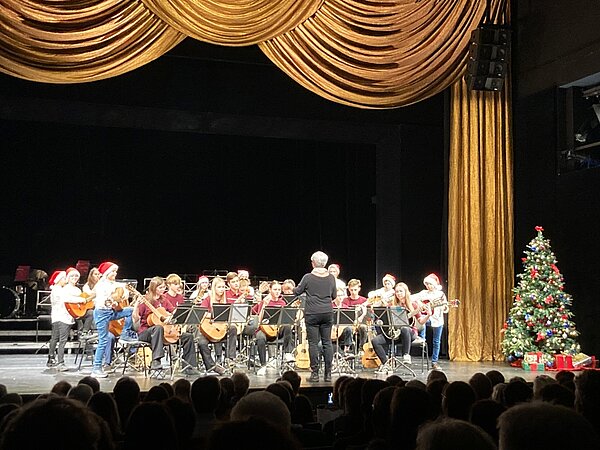 Das Gitarrenensemble steht auf der weihnachtlich geschmückten Bühne der Landesbühnen und spielt vor Publikum.
