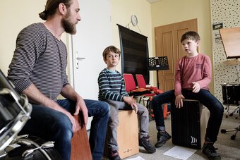 Zwei Percussion Schüler und ihr Lehrer spielen jeweils auf einer Cajon.