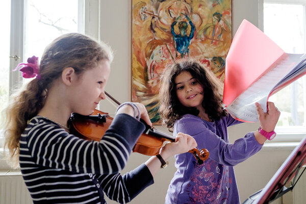 Ein Mädchen spielt Geige, während ein anderes Mädchen die Noten hält.