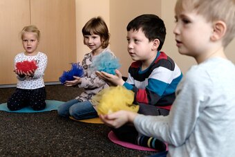 Vier Kinder der Früherziehung sitzen im Halbkreis und halten zusammengeknüllte bunte Tücher in den Händen.