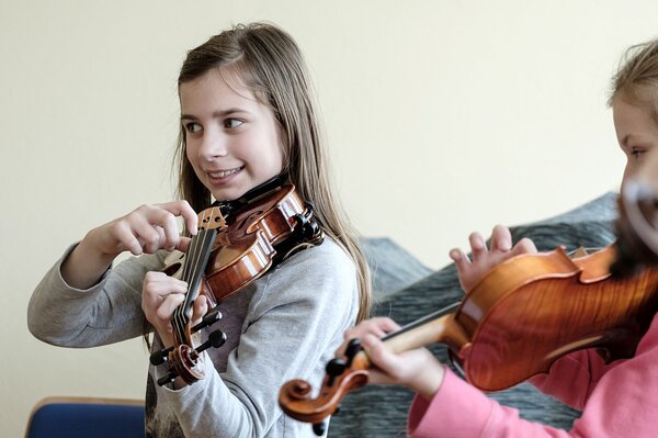 Zwei Mädchen zupfen die Saiten der Geige.