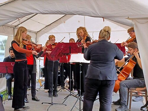 Das Großenhainer Streichorchester „Saitensprung“ steht in einem Festzelt und musiziert.