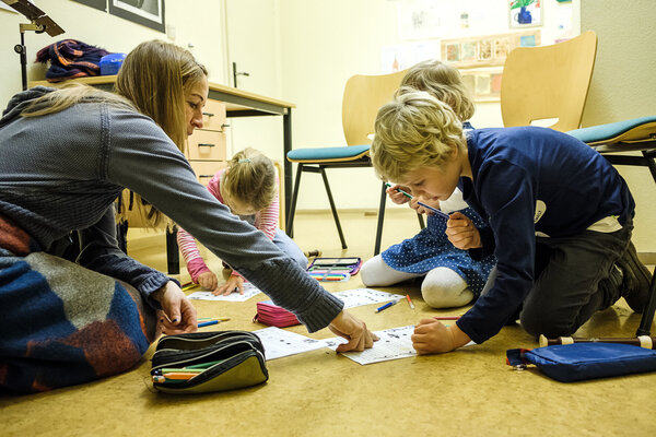 Drei Kinder und ihre Lehrerin sitzen auf dem Fußboden und malen Noten aus.