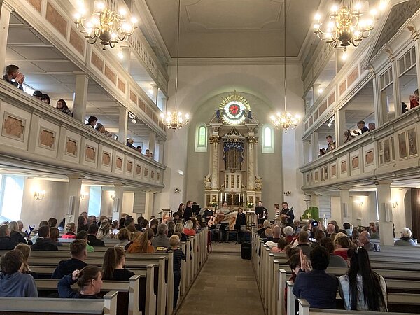 Es ist der Innenraum der Stadtkirche Nossen zu sehen, mit Publikum welches sich ein Gitarrenkonzert anschaut.