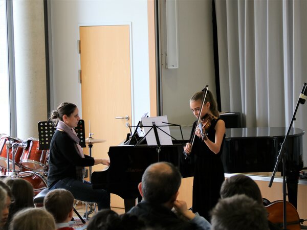 Eine Violinschülerin spielt ein Stück und ihre Lehrerin begleitet sie.