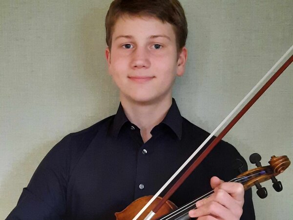 Ein Schüler mit seiner Geige ist auf dem Bild zu sehen.