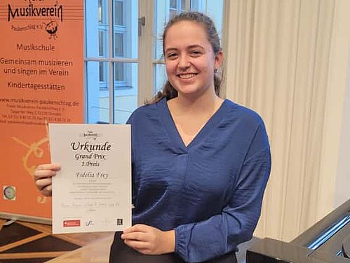 Freudestrahlend hält eine Klavierschülerin ihre Urkunde neben sich in die Kamera.