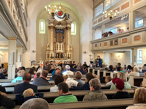 Ein Gitarrenkonzert im Kirchensaal vor dem beleuchteten Altar mit mehreren Schülern und vielen Zuschauern auf den Bänken.