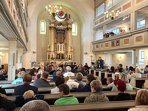 Ein Gitarrenkonzert im Kirchensaal vor dem beleuchteten Altar mit mehreren Schülern und vielen Zuschauern auf den Bänken.