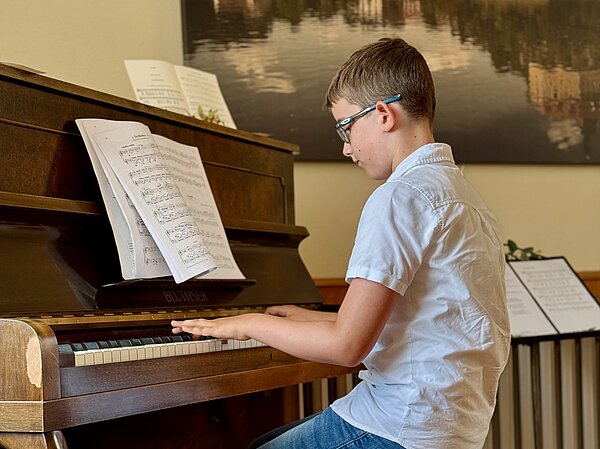 Ein Klavierschüler sitzt am Klavier und spielt.