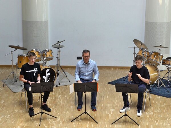 Es sitzen drei Percussionisten in Aktion vor zwei Schlagzeugen.