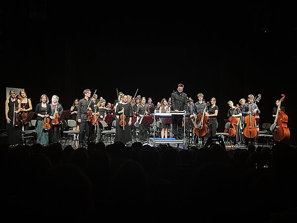 Das Jugendsinfonieorchester Radebeul steht auf der Bühne der Landesbühnen Sachsen, während das Publikum begeistert applaudiert.