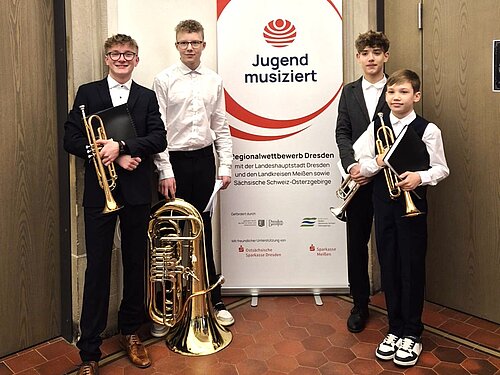 Vier Blechblasschüler mit ihren Instrumenten stehen vor und neben dem Banner von "Jugend musiziert".