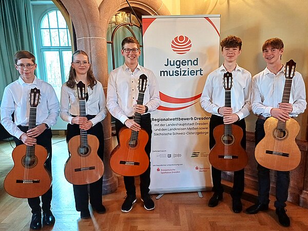 Das Gitarrenquintett aus Riesa posiert mit ihren Gitarren links und rechts neben dem Banner von "Jugend Musiziert".