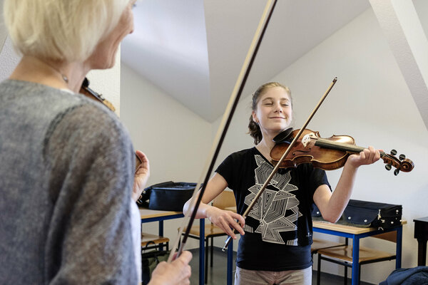 Eine Violinschülerin spielt auf ihrem Instrument, während ihre Lehrerin ihr spielen beobachtet.