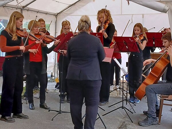 Das Großenhainer Streichorchester „Saitensprung“ steht in einem Festzelt und musiziert.