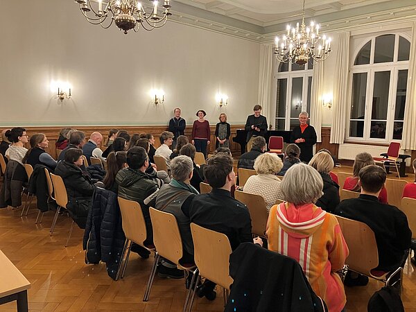 Ein festlicher Musikschulsaal, voll besetzt. Vorne sprechen Menschen, ein Klavier steht bereit – Konzertstimmung.