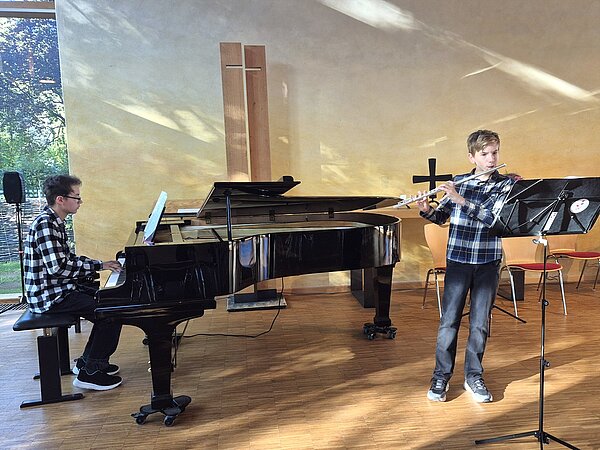 Ein junger Musikschüler spielt Querflöte, während er von einem anderen Musikschüler am Flügel begleitet wird.