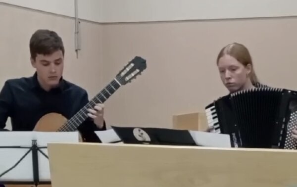 Gemeinsam musizieren ein Gitarrenschüler und eine Akkordeonschülerin.