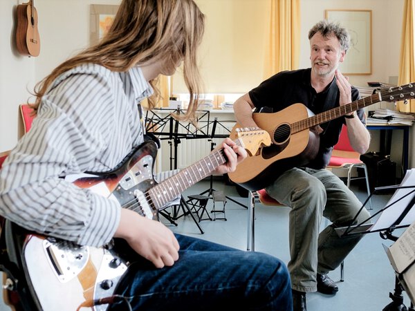 Ein Gitarrenlehrer zeigt seinem Schüler wie es besser geht.
