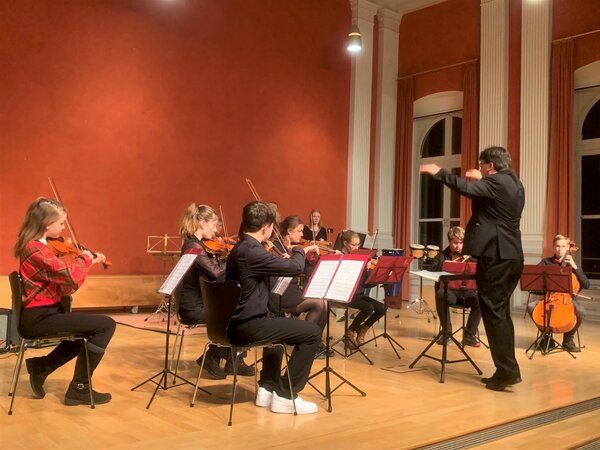 Ein Streichorchester mit Musikschülern und Dirigent spielt ein Stück.