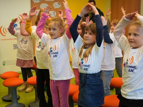 Die Kinder des Kinderchores haben die Hände in der Luft und schauen wie es weiter geht.