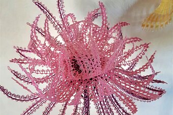 Es ist eine geklöppelte rosa Blume zu sehen.