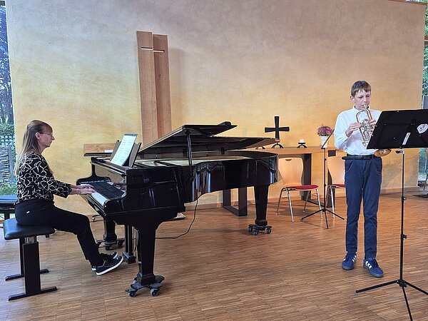 Ein junger Musikschüler spielt Trompete, während er am Flügel begleitet wird.