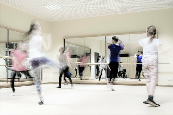 Kinder tanzen vor einem Spiegel mit Ballettstange durch den Raum.