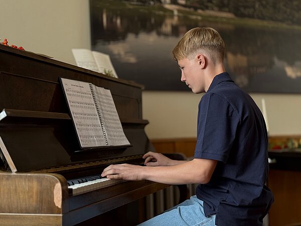 Ein Klavierschüler sitzt am Klavier und spielt.