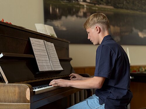 Ein Klavierschüler sitzt am Klavier und spielt.