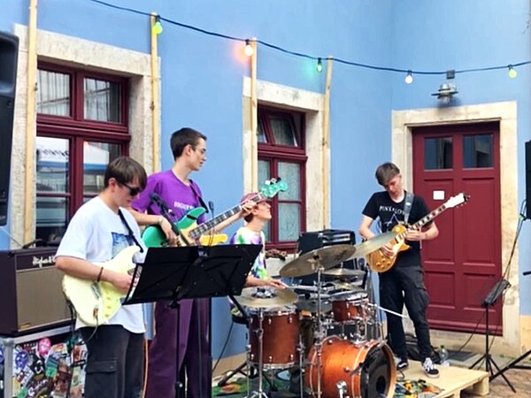 Die Band Jaetal musiziert zum Weinfest in Radebeul. Zu sehen sind Schüler die Gitarre, Bass und Schlagzeug vor einer Haus Wand mit Fenster spielen.