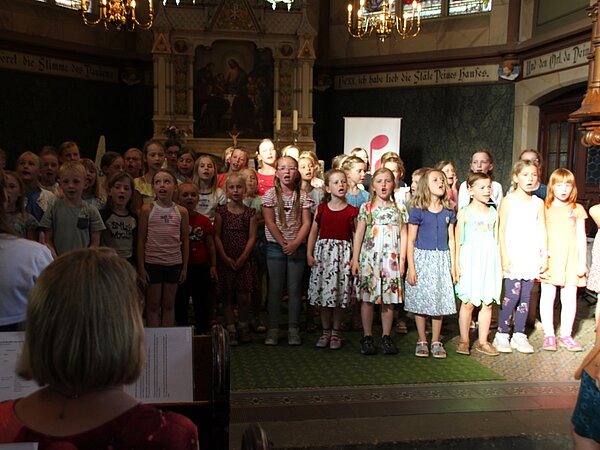 Der Kinderchor singt stehend im Altarraum der Kirche, vor Publikum.