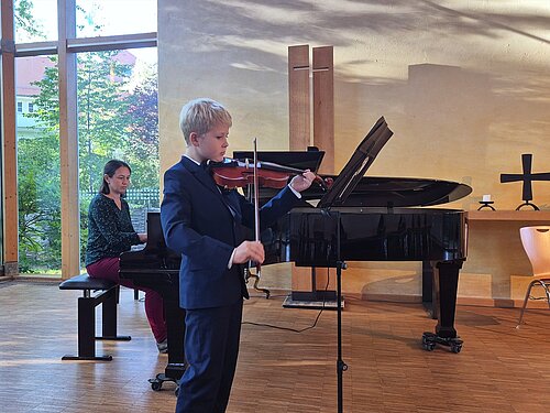 Ein Musikschüler spielt Geige, während er am Flügel begleitet wird.