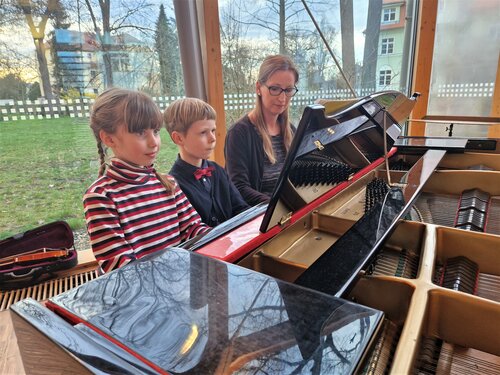 Zwei Klavierschüler und ihre Lehrerin spielen sechshändig am Klavier.