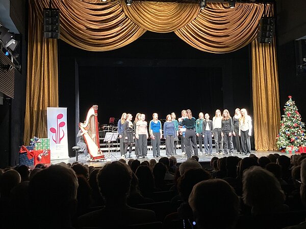 Ein Chor steht auf der weihnachtlich geschmückten Bühne der Landesbühnen und singt vor Publikum.